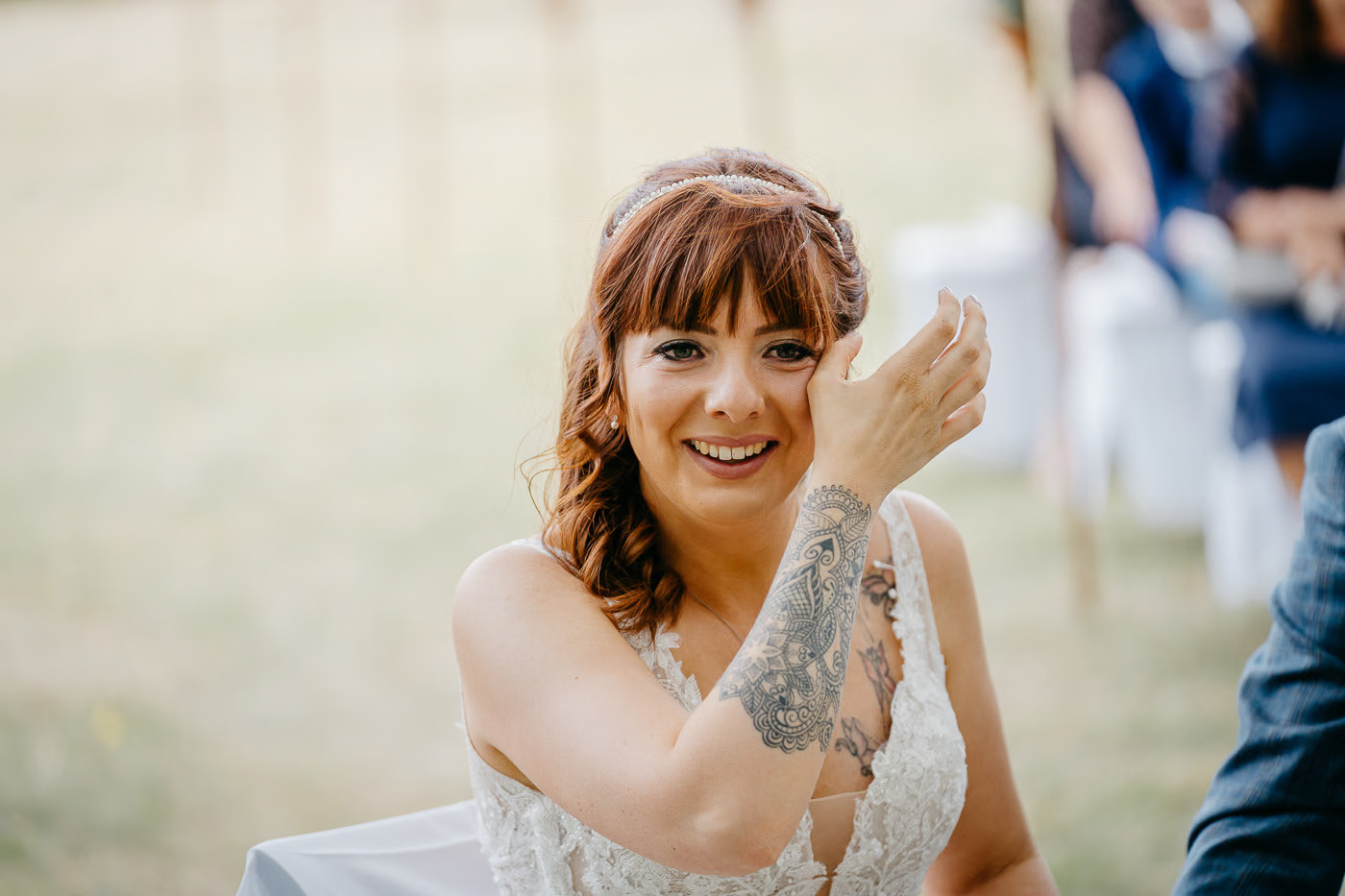 Freie Trauung Helmstedt – Braut mit roten Haaren und Diadem lächelt strahlend während der Zeremonie, Tattoo am Arm sichtbar, natürliche Hochzeitsreportage Helmstedt Kathrin Skorpel
