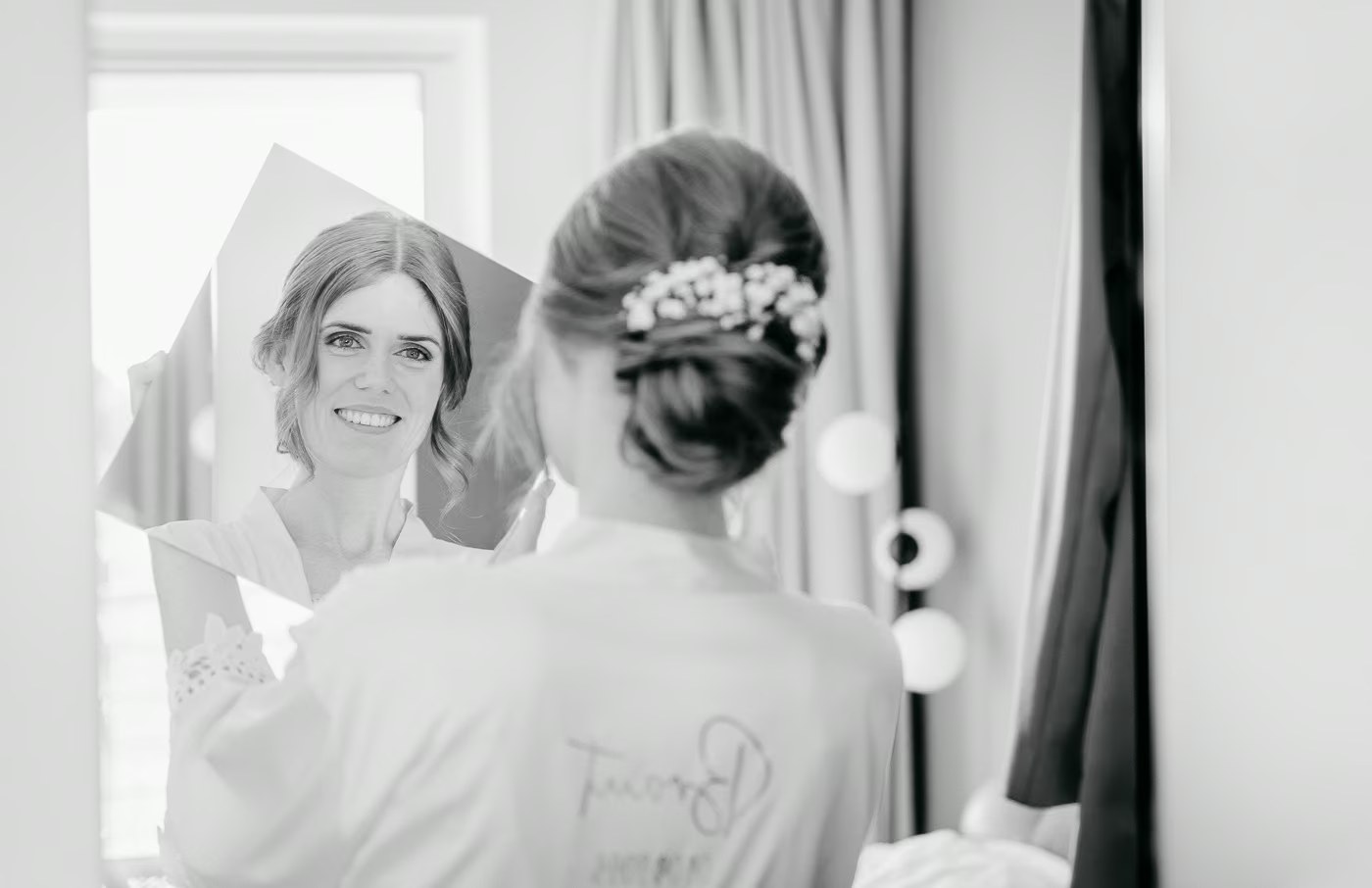 Getting Ready Hochzeit – Braut blickt lächelnd in den Spiegel, fertige Hochzeitsfrisur mit Blumenschmuck, emotionaler Moment, Hochzeitsfotos Emmerstedt Kathrin Skorpel