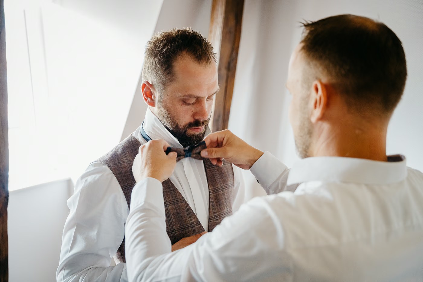 Getting Ready Hochzeit – Fliege des Bräutigams wird von einem Freund gebunden, herzlicher Moment zwischen Männern, Hochzeitsfotos Burg Warberg Kathrin Skorpel