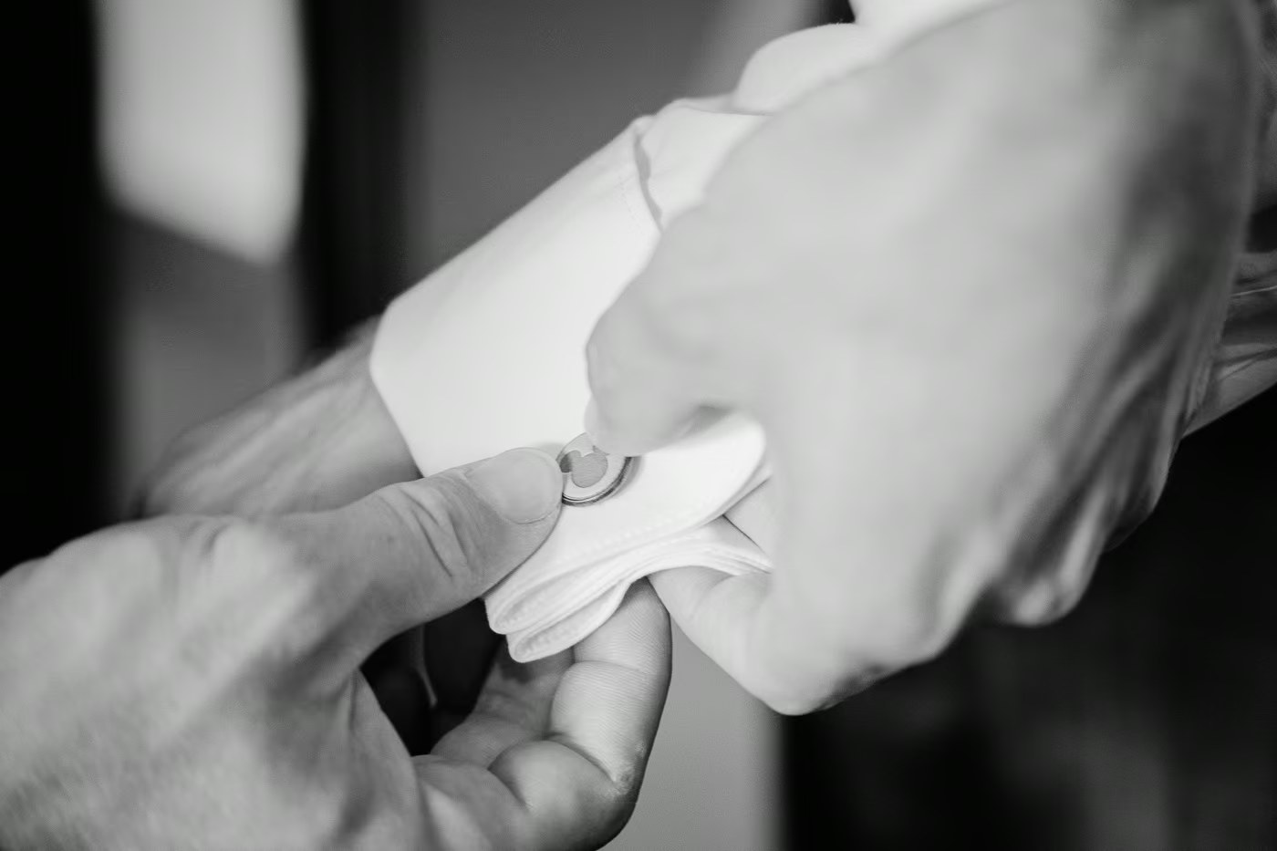 Getting Ready Hochzeit – Manschettenknopf wird am Hemd des Bräutigams befestigt, elegantes Schwarz-Weiß Detailfoto, Hochzeitsreportage Sickte Kathrin Skorpel