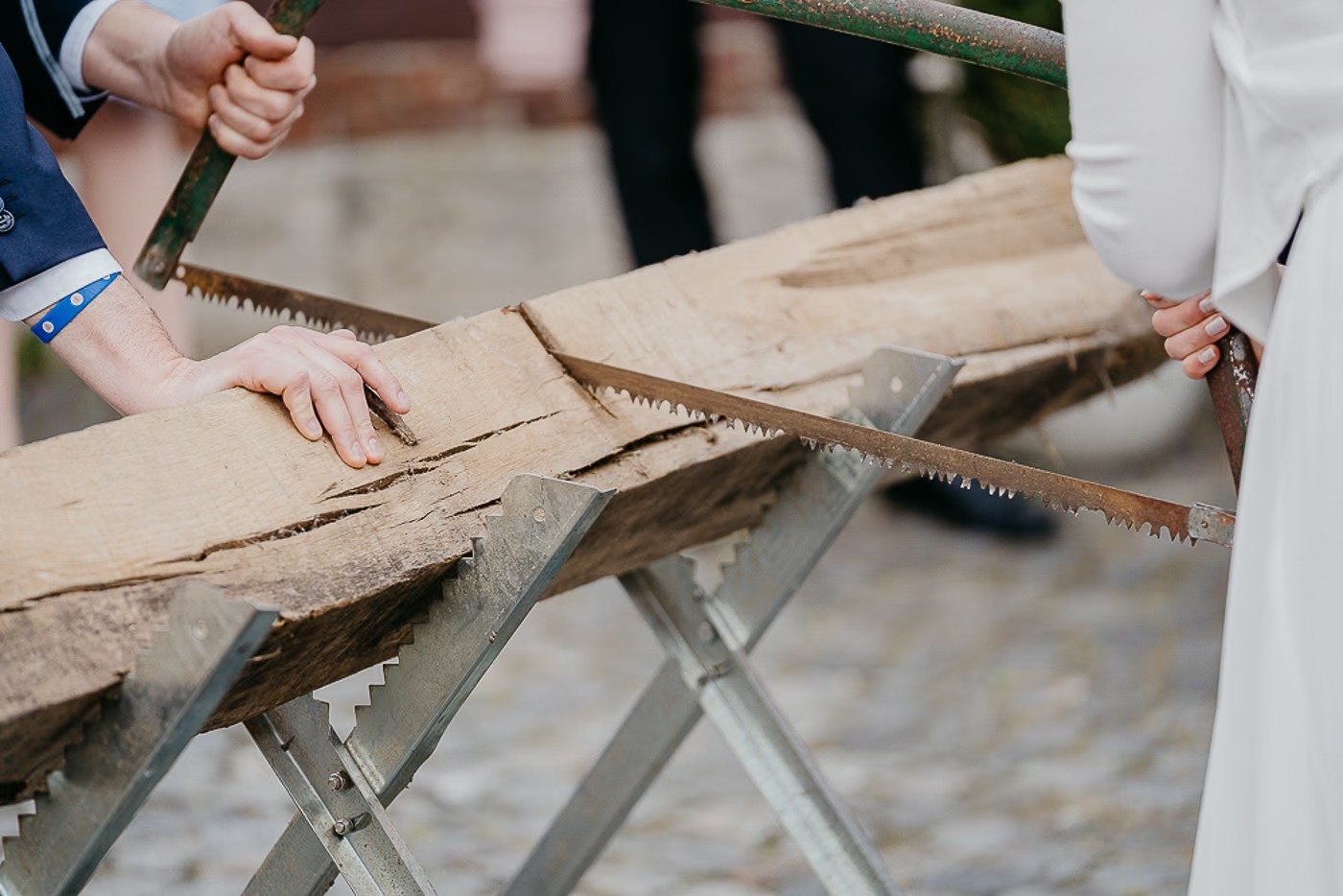 Hochzeitsfeier Schöningen – Brautpaar beim traditionellen Baumstammsägen, ausgelassene Stimmung unter den Gästen, Hochzeitsfotografie Schöningen Kathrin Skorpel