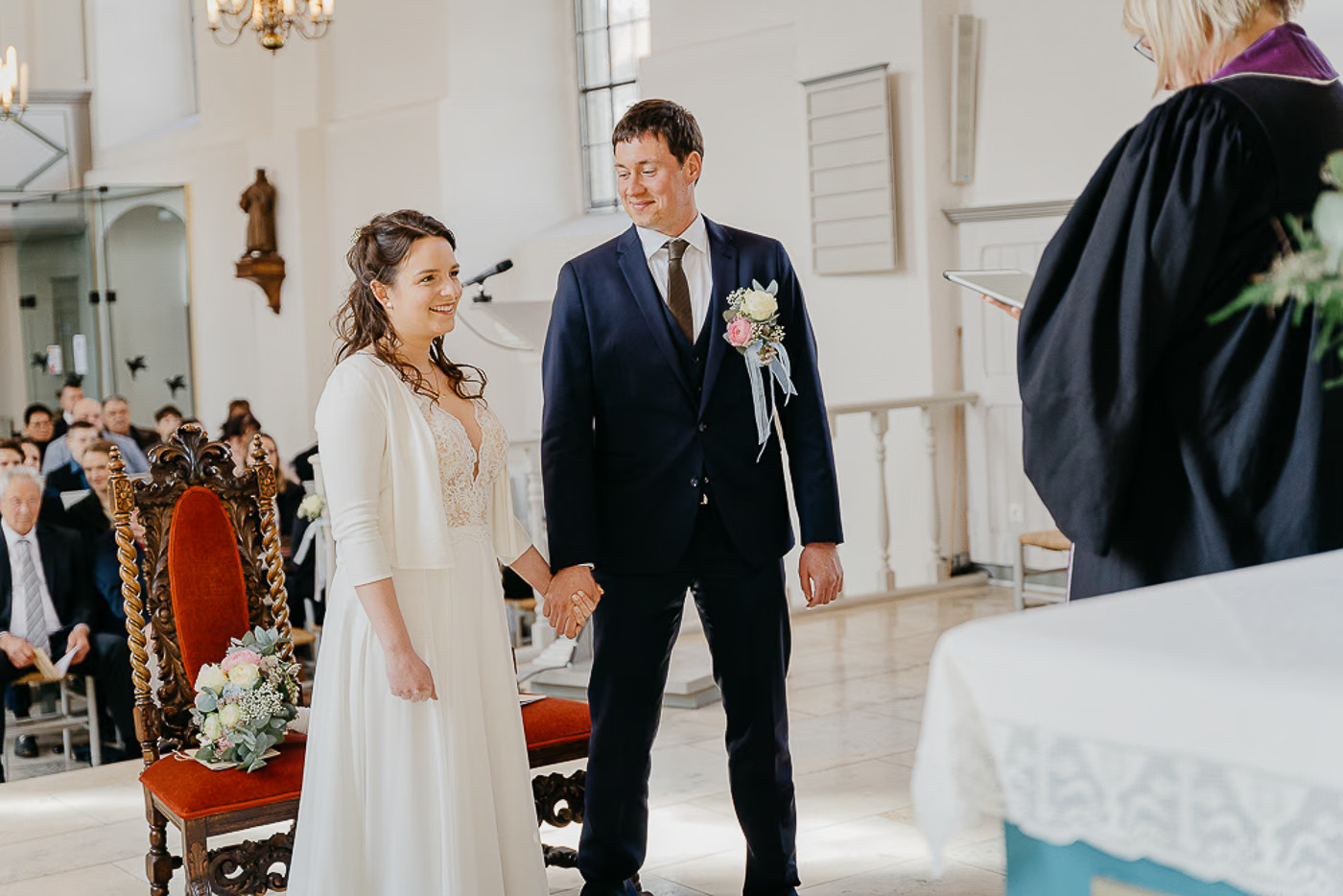 Kirchliche Trauung Helmstedt – Brautpaar steht Hand in Hand lächelnd vor der Pfarrerin am Altar, Gäste im Hintergrund, feierlicher Trauungsmoment Helmstedt Kathrin Skorpel