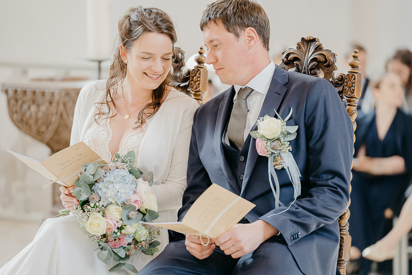 Kirchliche Trauung Peine – Braut und Bräutigam lesen gemeinsam im Trauungsheft und schauen sich liebevoll an, Brautstrauß mit blauen Hortensien, inniger Moment kirchliche Hochzeit Peine Kathrin Skorpel