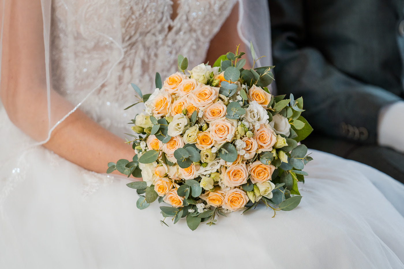 Kirchliche Trauung Wolfenbüttel – Nahaufnahme des Brautstraußes mit apricotfarbenen Rosen und Eukalyptus auf dem Brautkleid, florales Hochzeitsdetail Wolfenbüttel Kathrin Skorpel