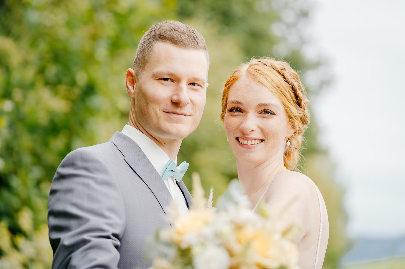 Paarshooting Bad Harzburg – Brautpaar blickt gemeinsam lächelnd in die Kamera, Bräutigam mit mintfarbener Fliege, Braut mit roten Haaren und Flechtfrisur, herzliche Verbundenheit, Hochzeitsfotografie Bad Harzburg Kathrin Skorpel