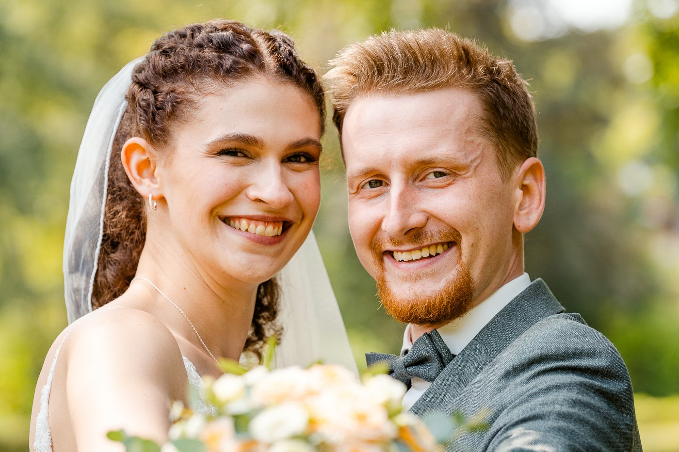 Paarshooting Helmstedt – Brautpaar lächelt direkt in die Kamera, Brautstrauß unscharf im Vordergrund, fröhliche unmittelbare Ausstrahlung, Hochzeitsfotografie Helmstedt Kathrin Skorpel