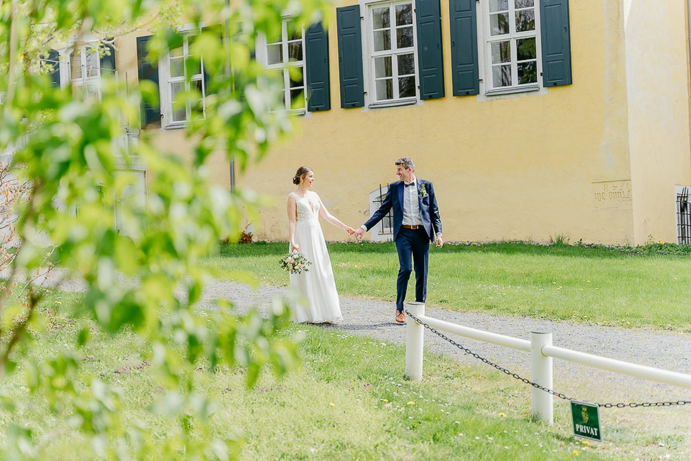 Paarshooting Schlosspark Cremlingen – Brautpaar geht Hand in Hand über die Wiese vor dem gelben Schloss mit dunkelgrünen Fensterläden, unbeschwerter gemeinsamer Spaziergang, Hochzeitsfotografie Schlosspark Cremlingen Kathrin Skorpel