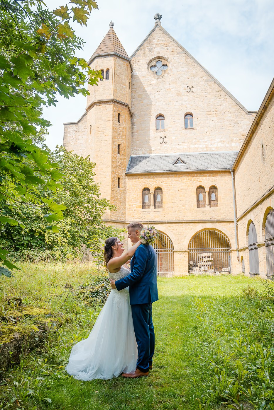 Paarshooting Kaiserpfalz Goslar – Brautpaar umarmt sich zärtlich vor der historischen Sandsteinfassade der Kaiserpfalz, Braut im weißen Tüllkleid, warmes Sommerlicht, Hochzeitsfotografie Kaiserpfalz Goslar Kathrin Skorpel