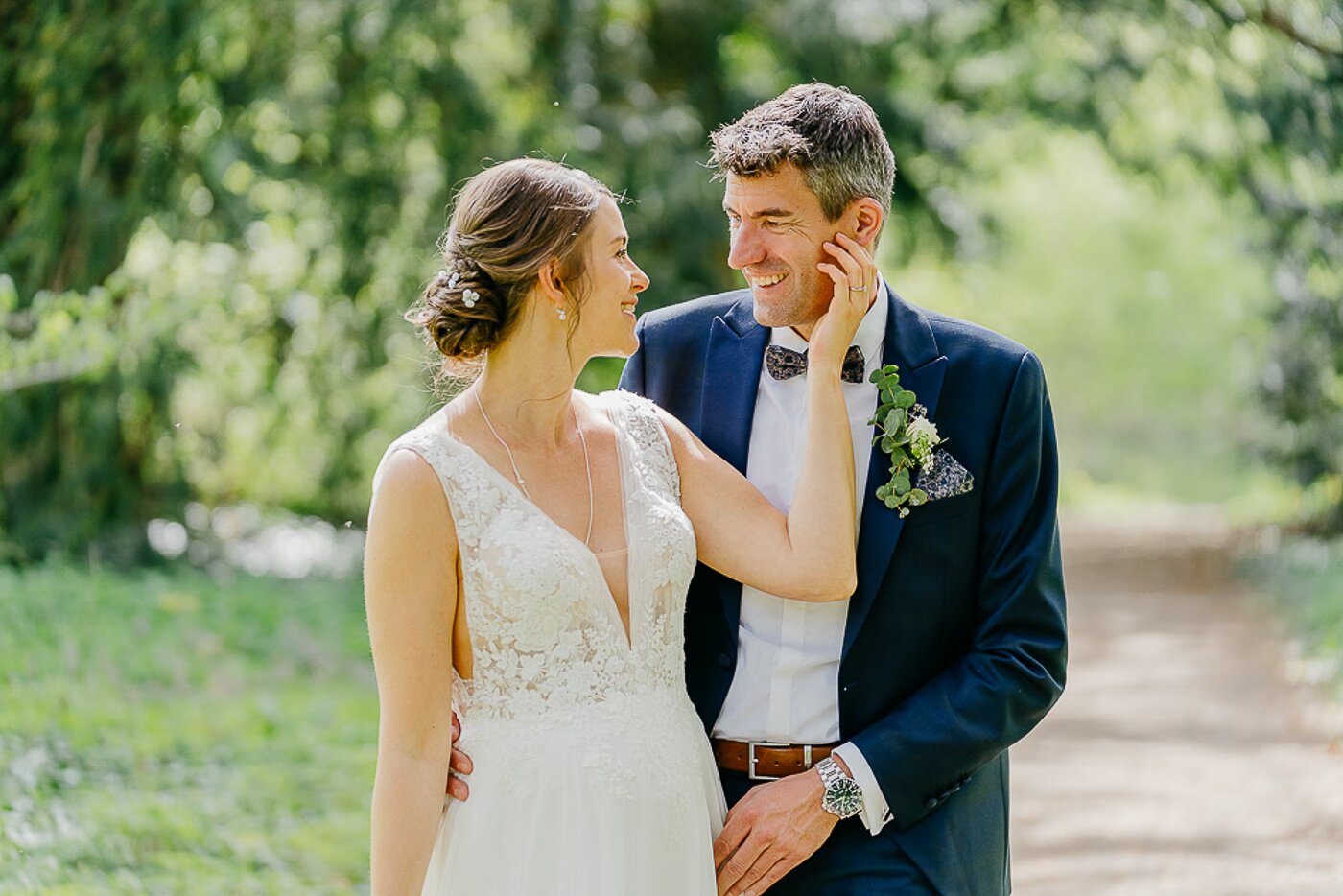 Paarshooting Cremlingen – Bräutigam hält lachend das Gesicht der Braut, verliebter Blick im grünen Schlosspark Cremlingen, natürliche Emotionen Hochzeitsfotografie Cremlingen Kathrin Skorpel