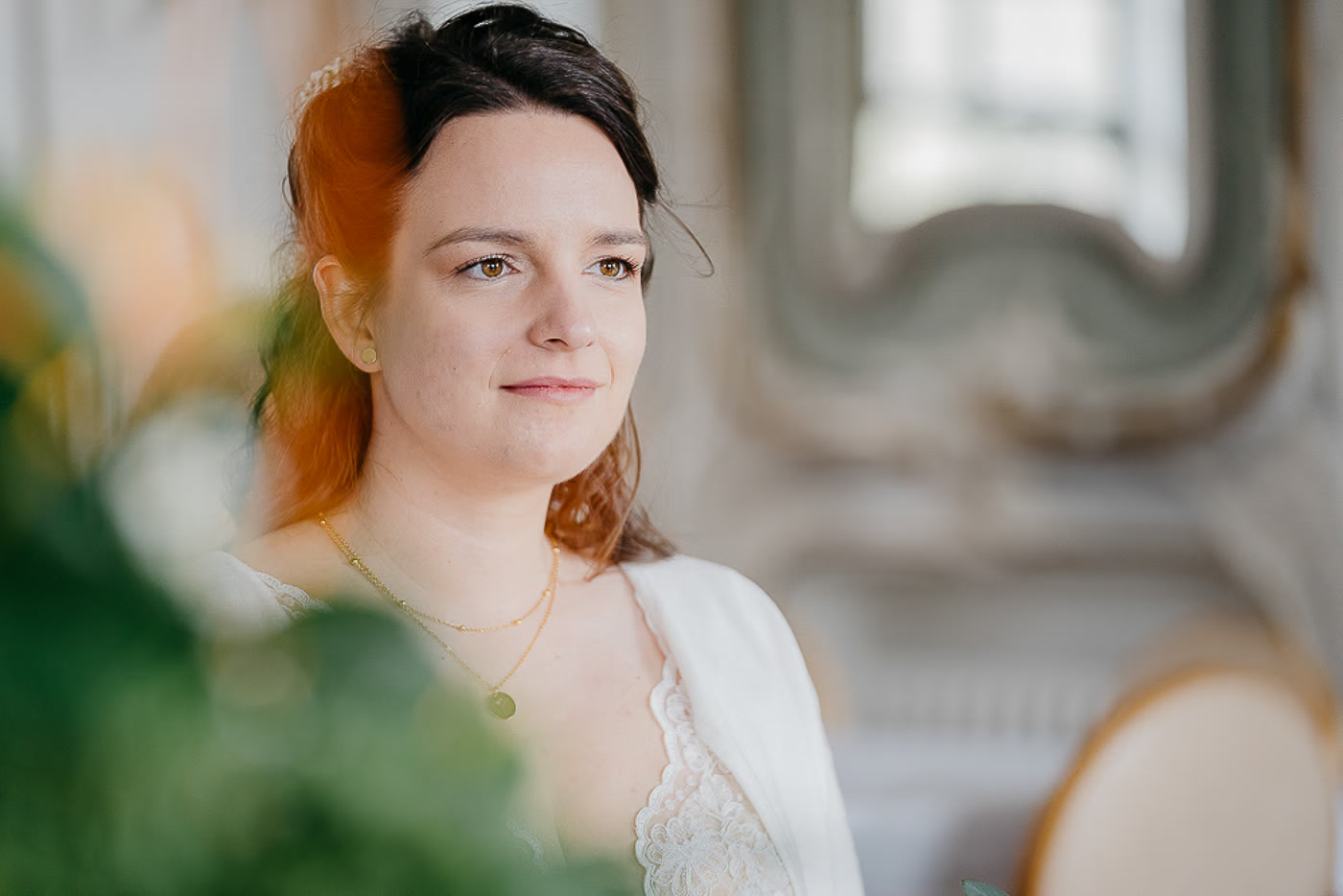 Standesamt Hochzeit Helmstedt – Nahaufnahme Braut mit träumerischem Blick, goldene Halskette, im Hintergrund ornamentierter Rokoko-Spiegel, stille Vorfreude kurz vor dem Ja-Wort, Hochzeitsfotos Helmstedt Kathrin Skorpel
