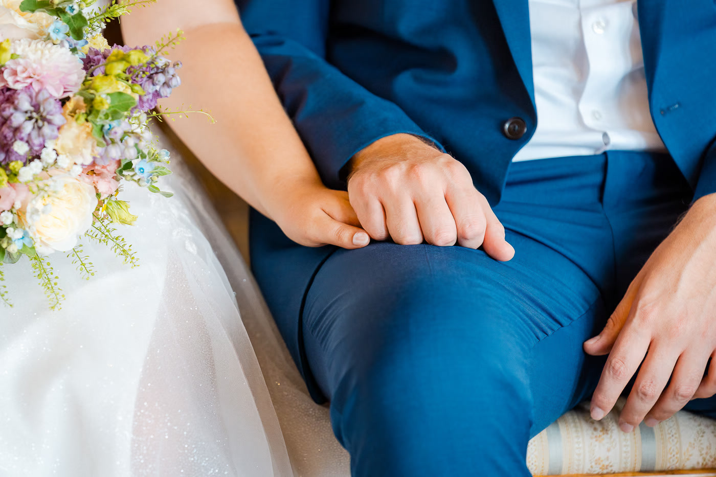 Standesamt Hochzeit Helmstedt – Detailaufnahme verschränkte Hände des Brautpaares während der Zeremonie, bunter Brautstrauß und blauer Hochzeitsanzug, stille Verbundenheit, Hochzeitsfotografie Helmstedt Kathrin Skorpel
